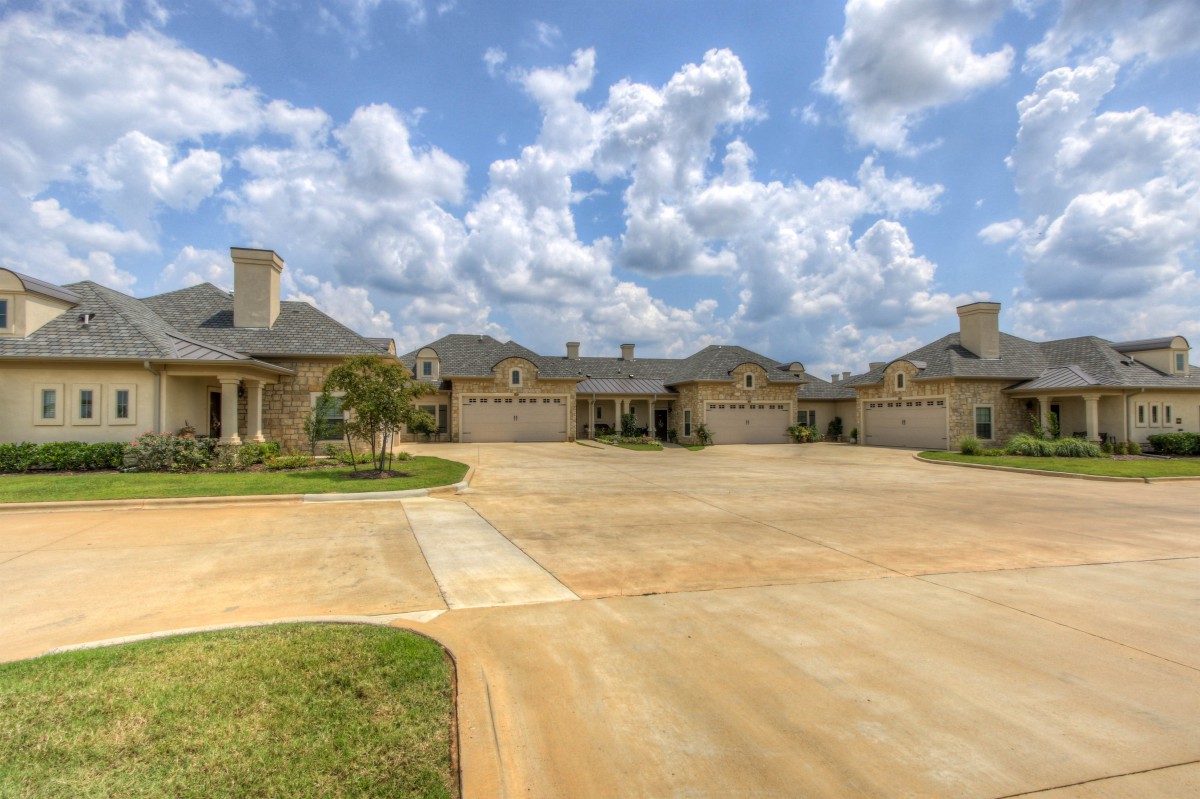 A view of a suburban residential area with multiple houses and a spacious driveway under a cloudy sky.