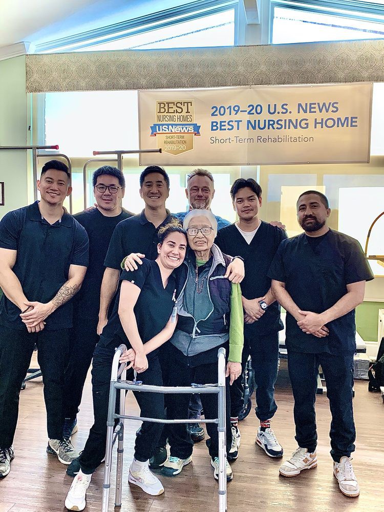 A group of healthcare staff posing with an elderly person, standing in front of a 'Best Nursing Home' award banner.