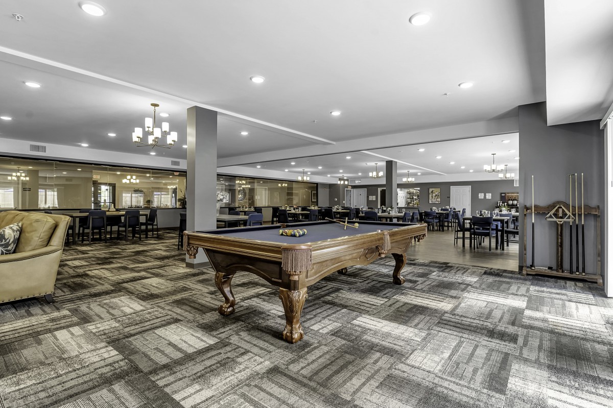 A spacious recreation room with a billiards table and modern seating arrangements.
