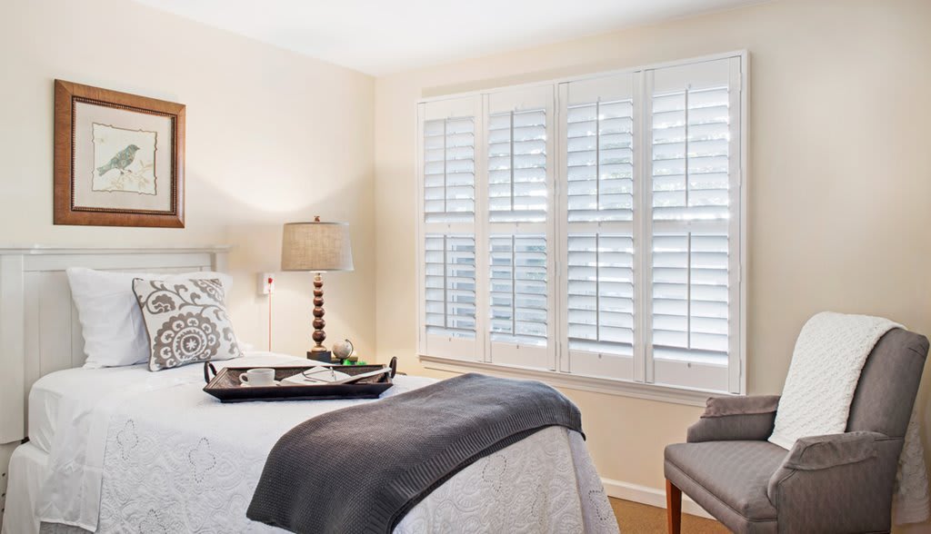 A cozy bedroom with elegant decor and natural light streaming through window shutters.
