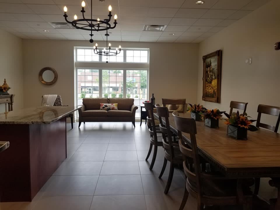 A well-lit dining area with a chandelier, tables and chairs, and a sofa near large windows.