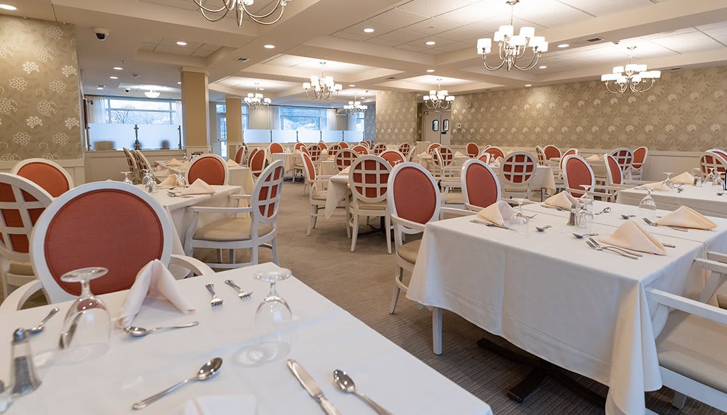 An elegant dining room with neatly arranged tables and chairs, featuring chandeliers and a classic interior design.