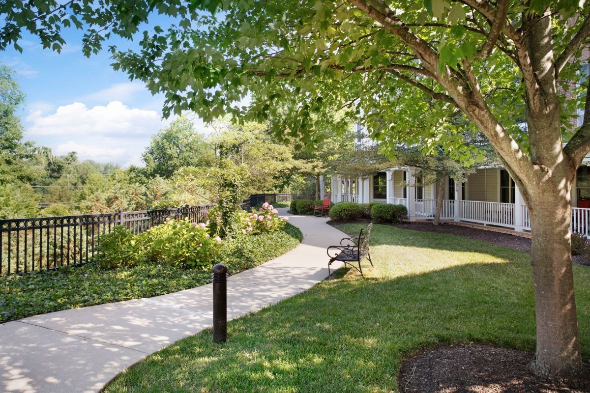 A serene garden pathway leading to a house, surrounded by trees and a well-maintained lawn.