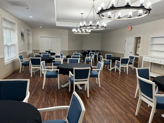 An empty dining or event space with neatly arranged tables and chairs, illuminated by chandeliers.