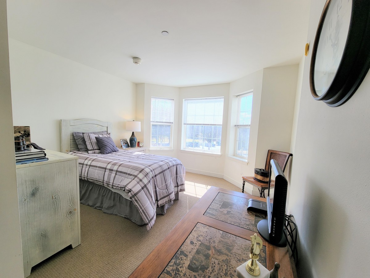 A bright bedroom with natural light, featuring a neatly made bed and cozy decor.