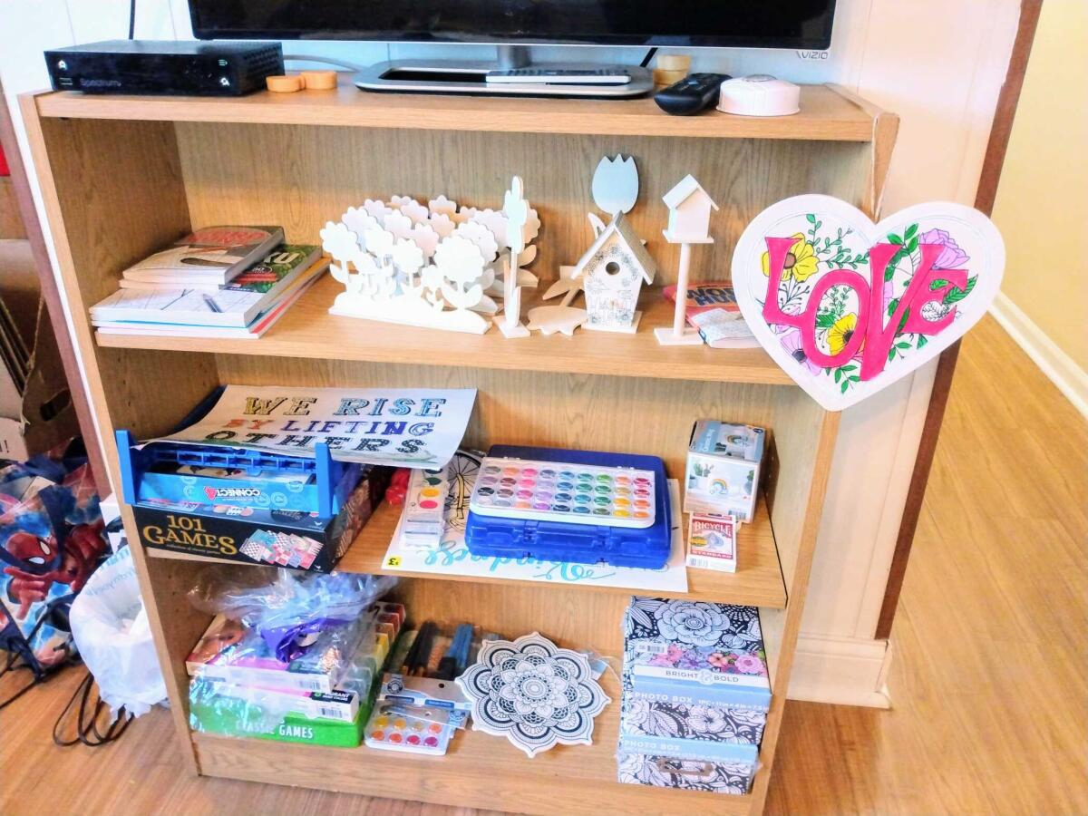 A wooden shelf displaying various craft supplies, including paints, puzzles, and wooden decorative items.