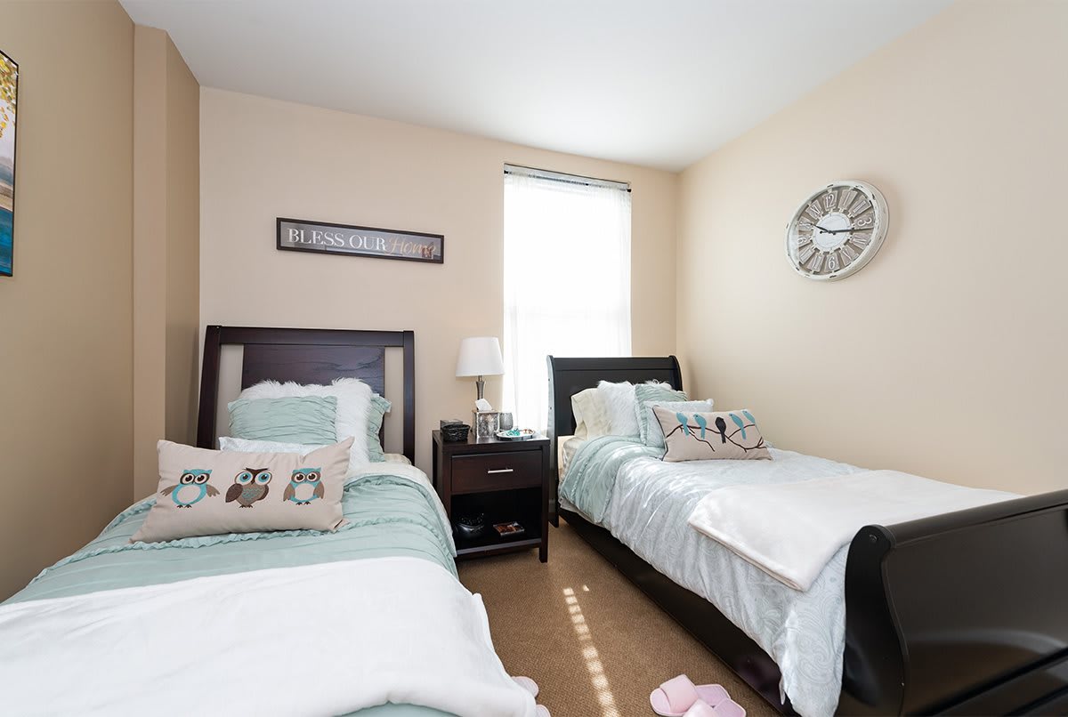 A cozy bedroom featuring two twin beds with decorative pillows and a central window.