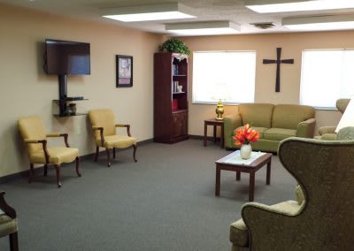 A waiting room with comfortable seating, a television, and a cross on the wall.