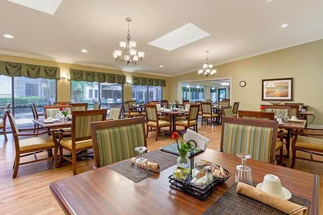 A spacious and elegant dining area with neatly arranged tables and chairs, featuring ambient lighting from chandeliers.
