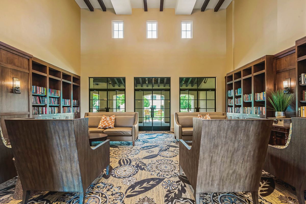 A modern living room with sofas, bookshelves, and decorative carpet, featuring high ceilings and multiple windows.