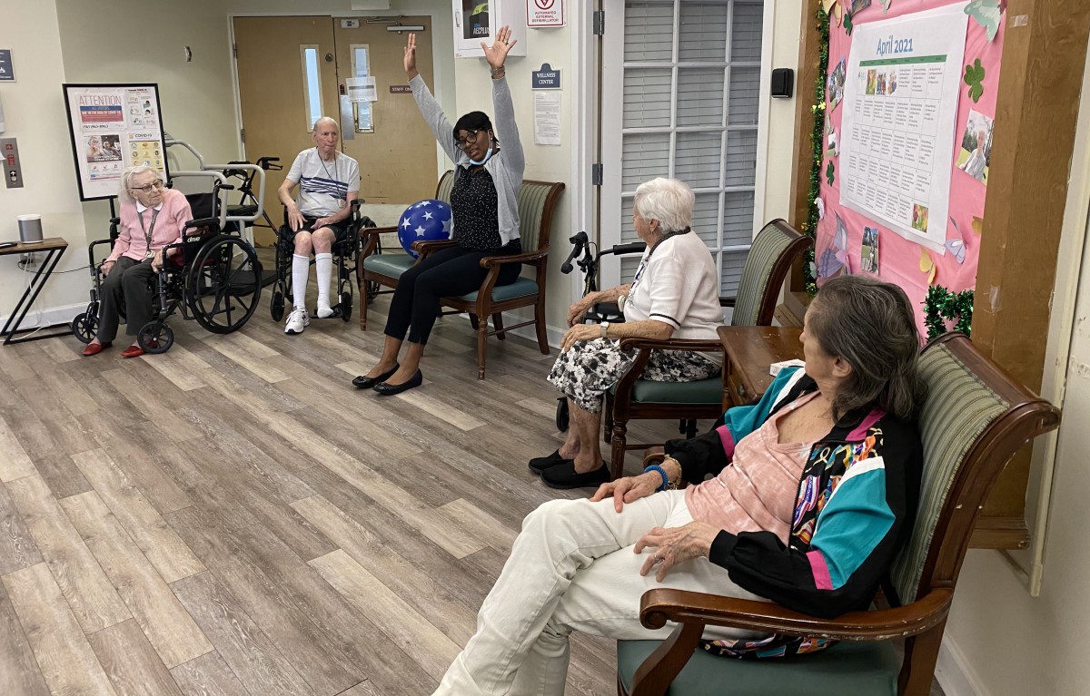A group of elderly individuals engaging in a seated exercise session indoors.