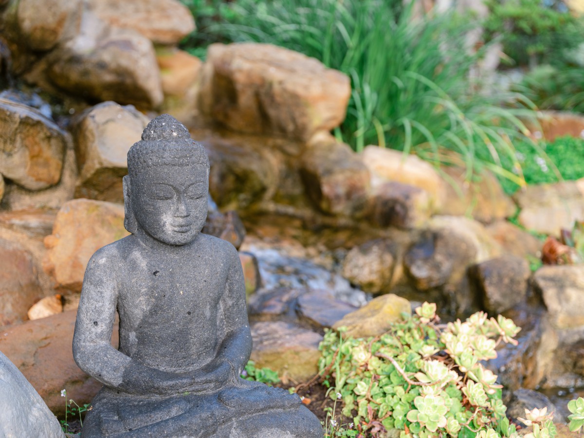 A serene Buddha statue in a tranquil garden setting with rocks and greenery.