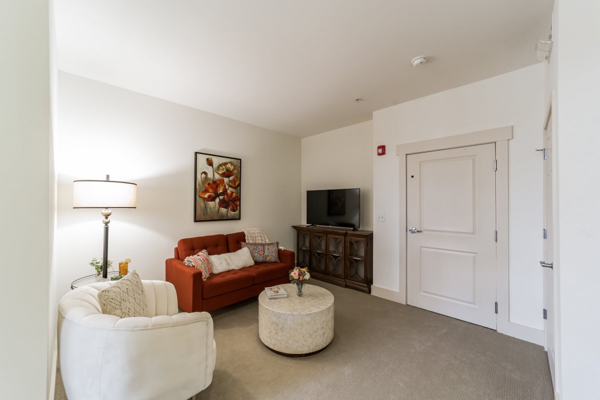 A cozy living room with a red sofa, armchair, television, and artwork on the wall.