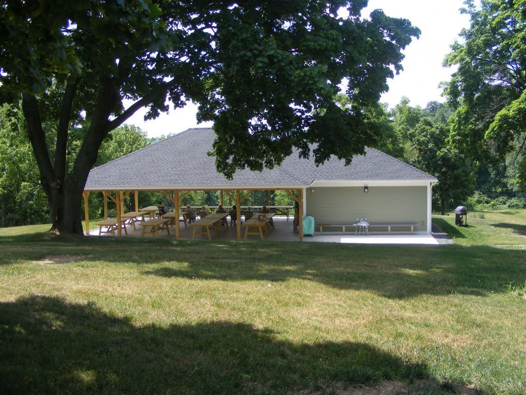 An outdoor pavilion surrounded by trees and grass in a park setting.