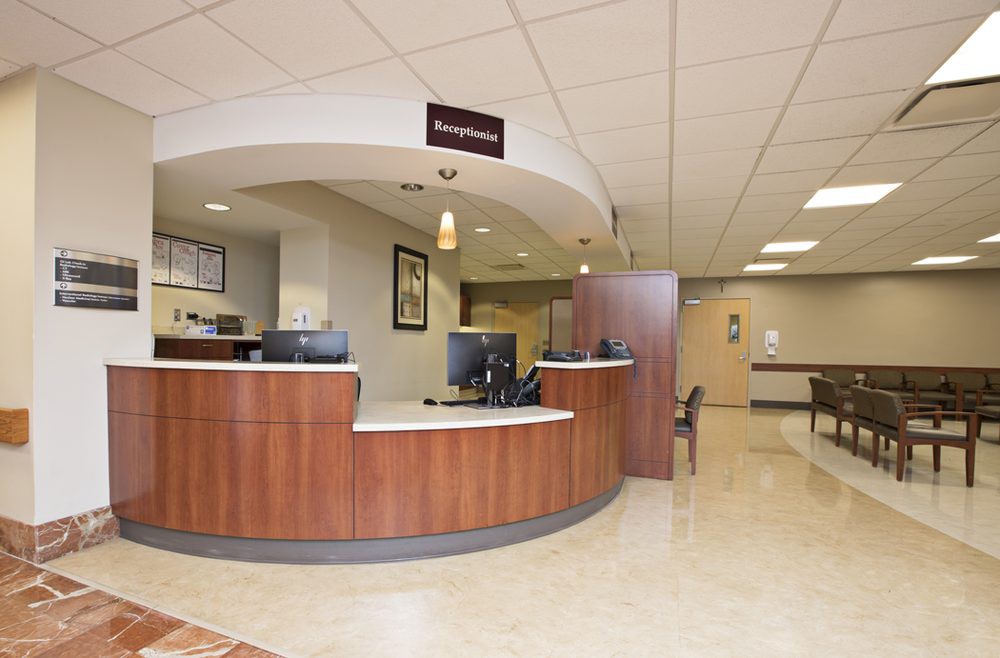 A hospital reception area with a curved desk and waiting room chairs.