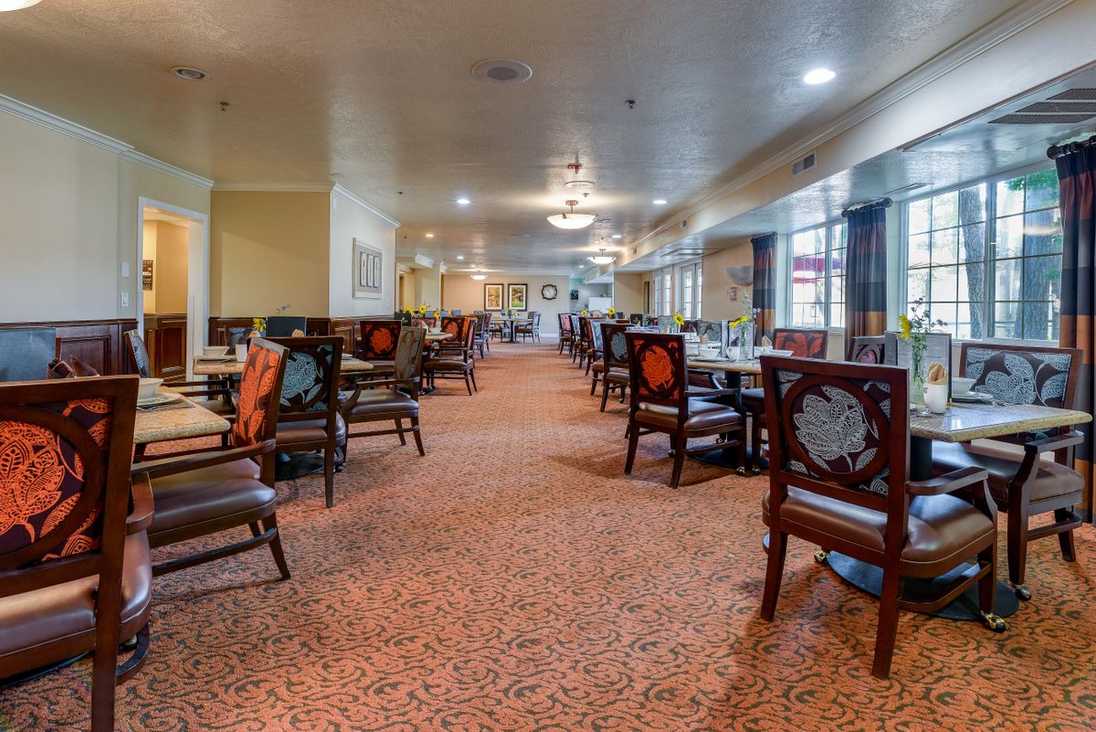 A spacious dining area with neatly arranged tables and chairs, featuring carpeted flooring and ambient lighting.