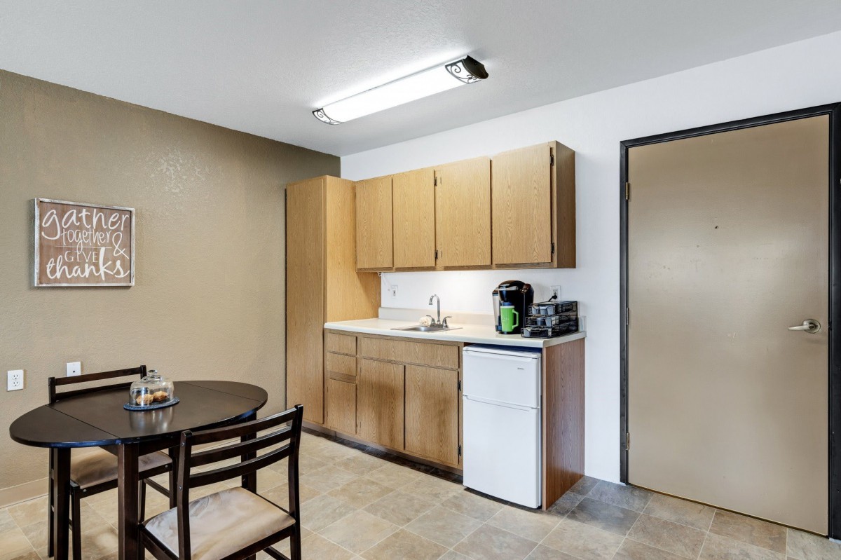 A simple kitchen setup with wooden cabinets, a small fridge, and a dining table.
