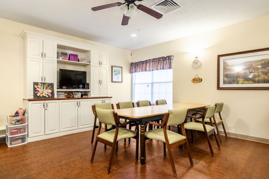 A cozy dining room with a long table and chairs, featuring built-in shelves, a ceiling fan, and a window allowing natural light.