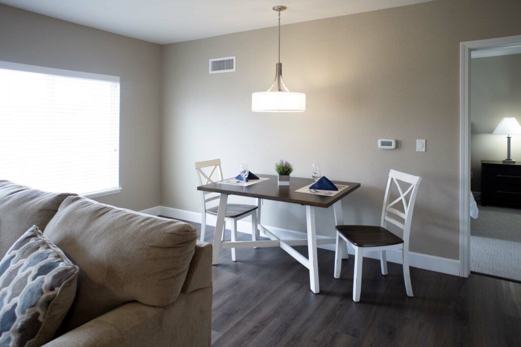 A modern and minimalist dining area with a wooden table, two chairs, and a pendant light.