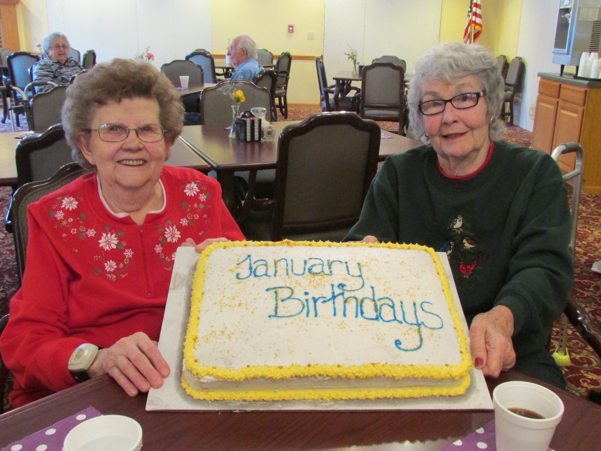 Two elderly women celebrating January birthdays with a large cake.