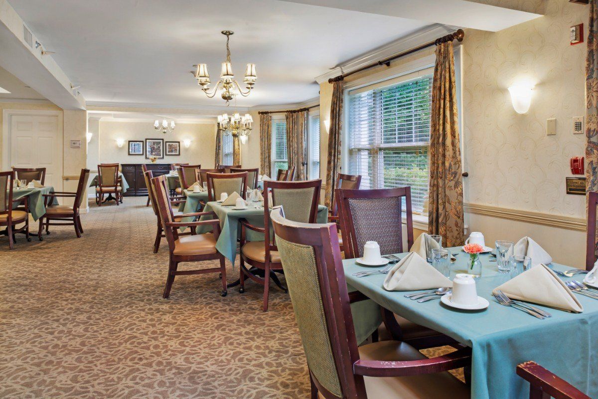 An elegantly set dining room with multiple tables and chairs, featuring large windows and decorative chandeliers.