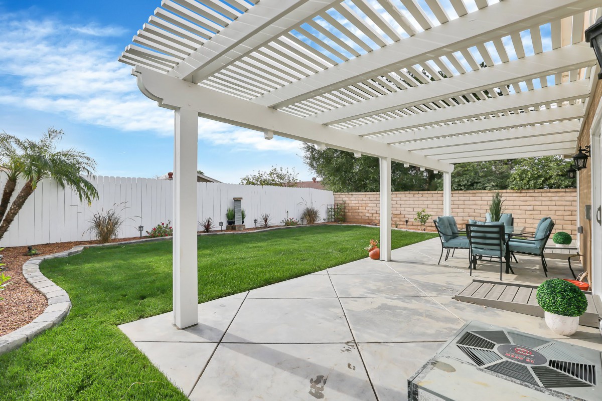 A backyard patio area with a pergola and outdoor furniture, featuring a well-maintained lawn.