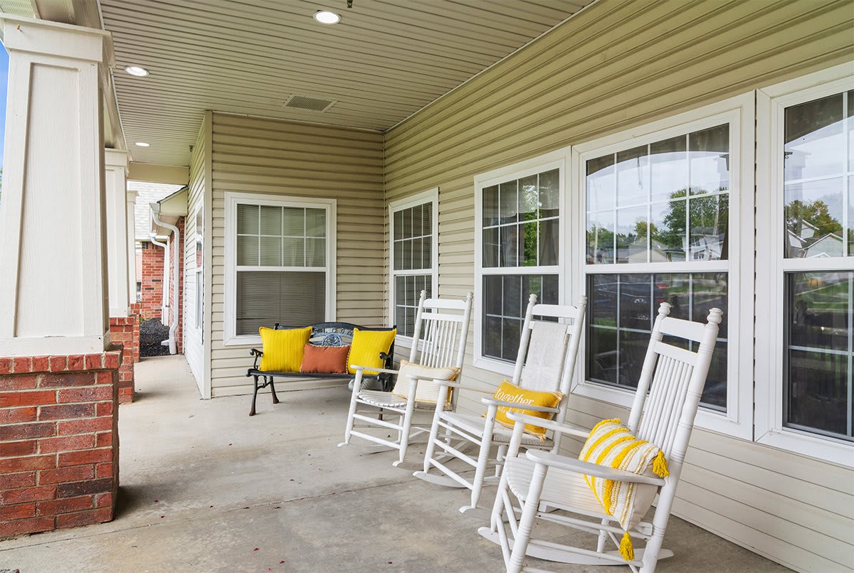 A cozy porch with white rocking chairs and a bench adorned with colorful cushions.