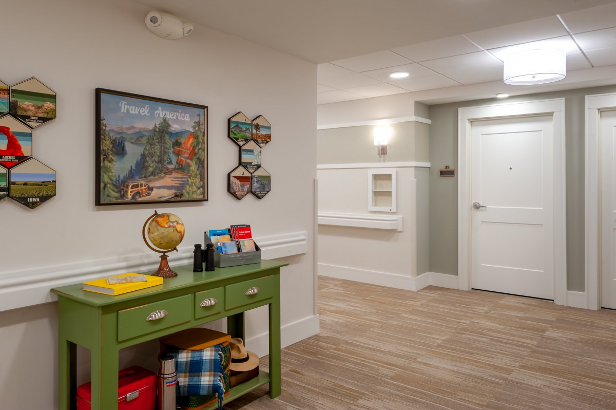 A cozy hallway featuring a green table with various decorative items, including a globe and books, along with wall art and wooden flooring.