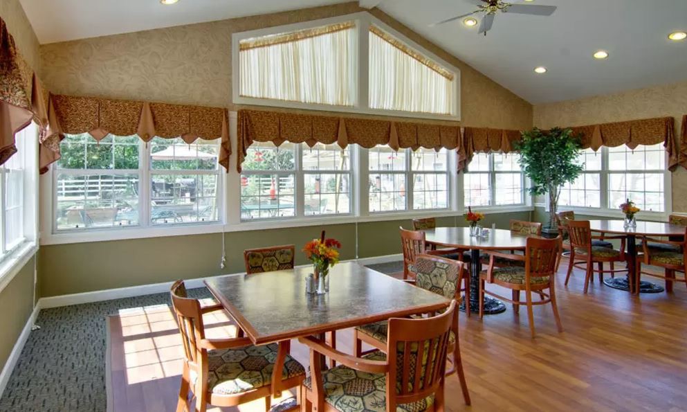 A well-lit dining area with tables and chairs, featuring large windows and curtains.