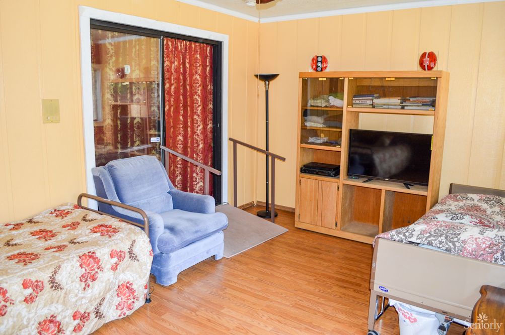 A cozy living room with a blue armchair, wooden bookshelf, and television on a hardwood floor.