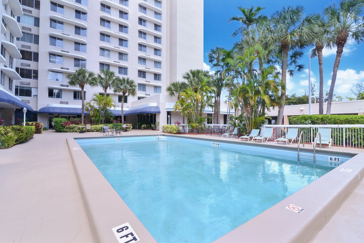 An outdoor swimming pool next to a hotel surrounded by palm trees.