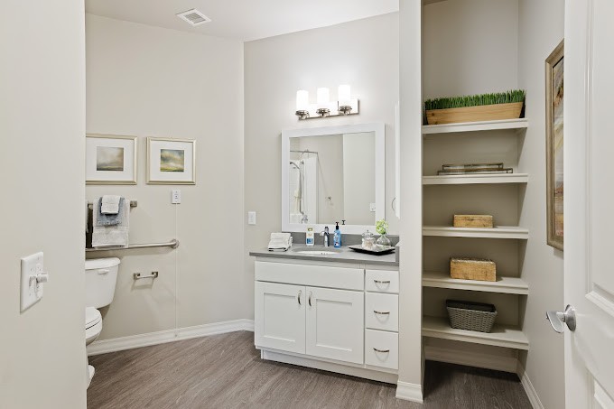 A modern bathroom with a white vanity, mirror, and open shelving.