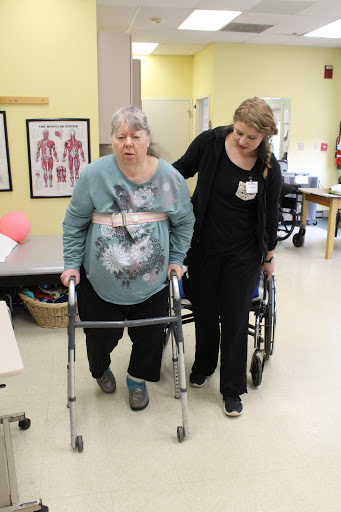 A healthcare professional assists an elderly woman using a walker during a rehabilitation session.