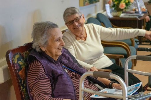 Two elderly women enjoying a joyful moment together in a care facility.