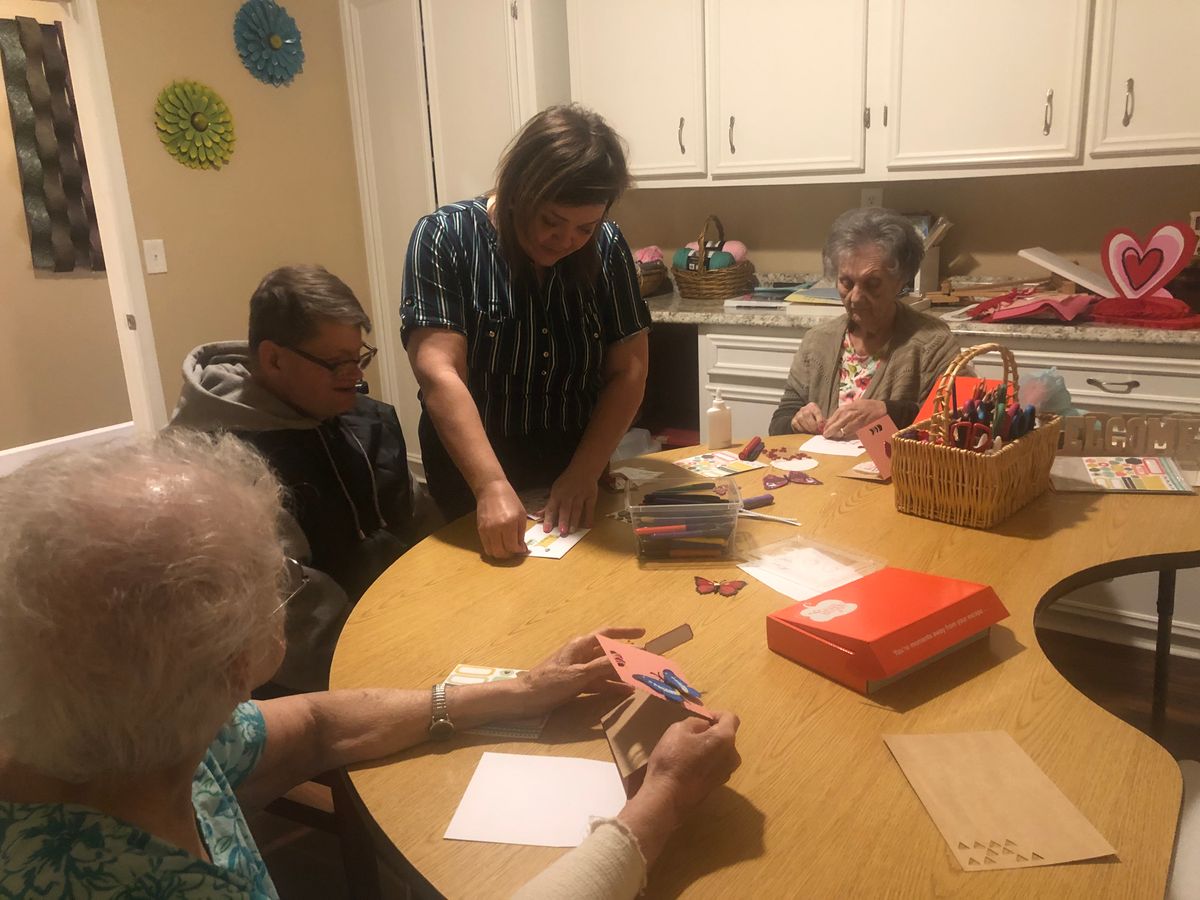 A group of elderly individuals engaged in a crafting activity around a table indoors.