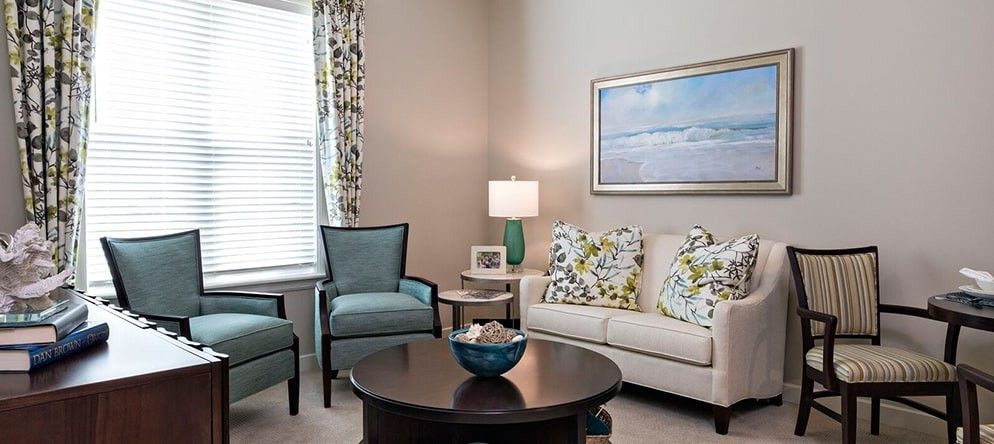A cozy living room featuring a sofa with patterned cushions, an armchair, and a coffee table accentuated by a lamp and framed artwork.