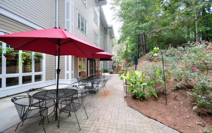 A charming outdoor patio area with tables and red umbrellas beside a landscaped garden path.