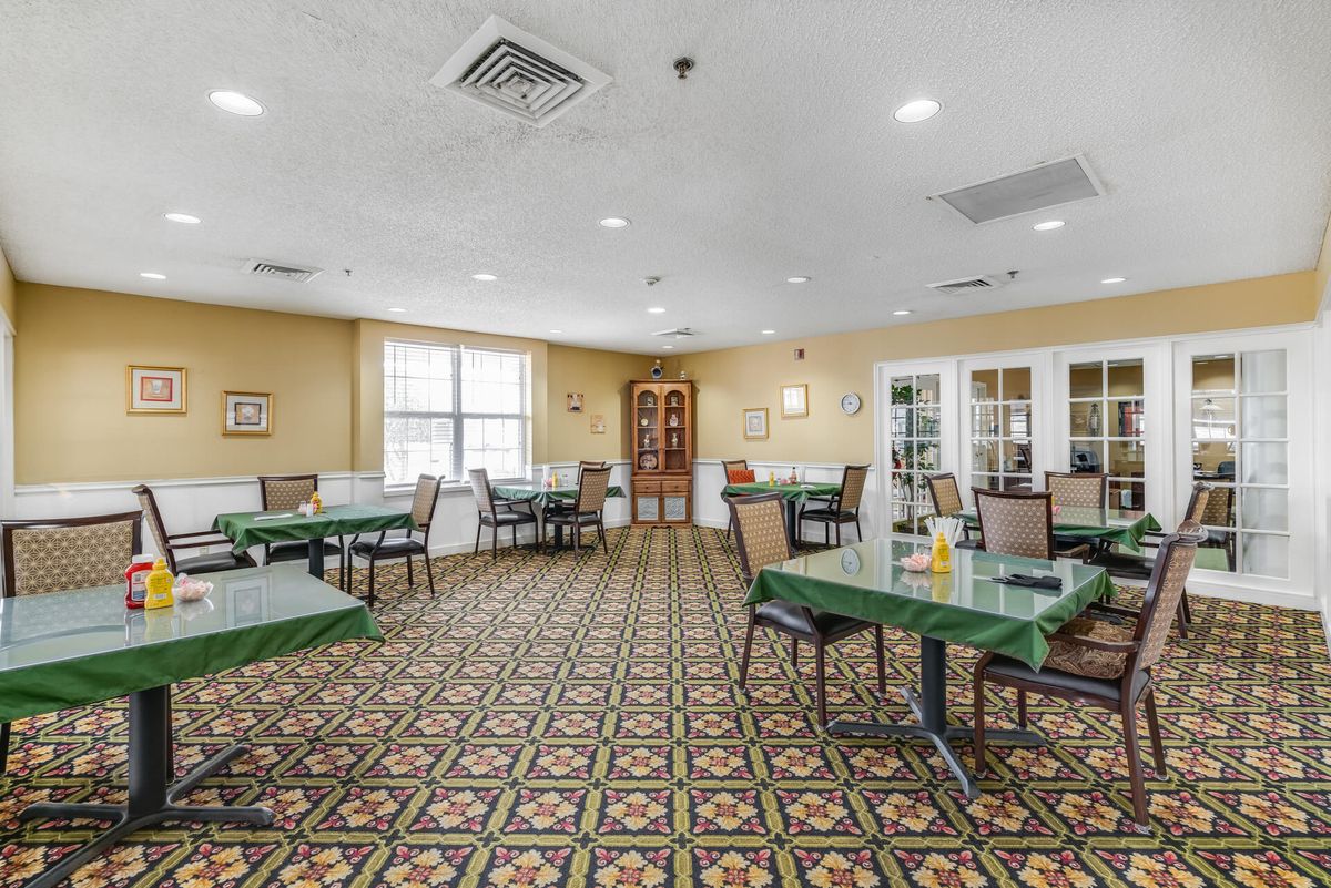 An empty dining room with tables and chairs arranged on a patterned carpet.