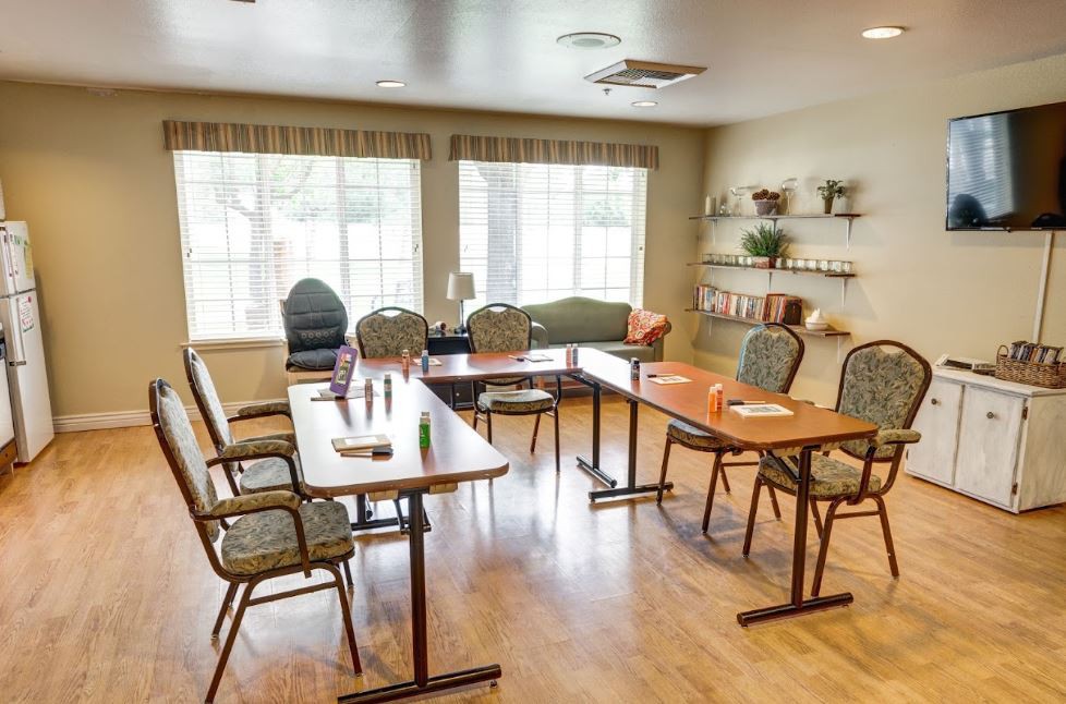 A bright meeting room with arranged tables and chairs, featuring large windows and decorative shelving.