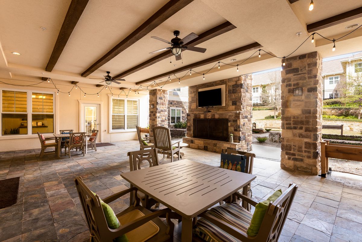 A cozy outdoor patio area featuring comfortable seating, ceiling fans, and a stone fireplace beneath a covered space.