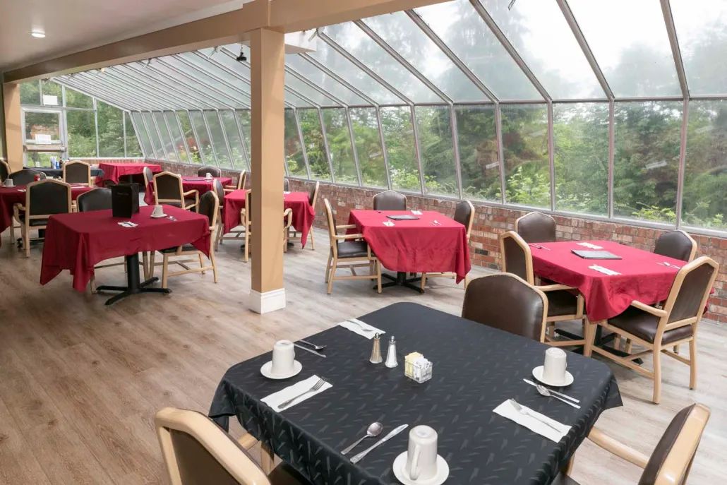 A bright restaurant interior with table settings and large windows overlooking the outdoors.