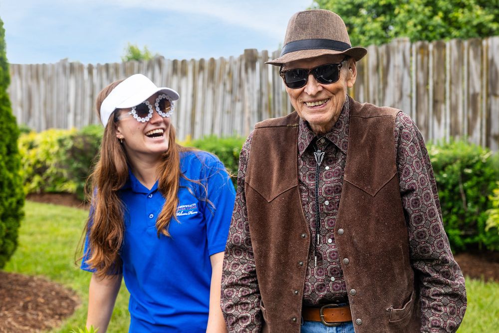 Two people enjoy a sunny day, smiling and wearing sunglasses and hats.