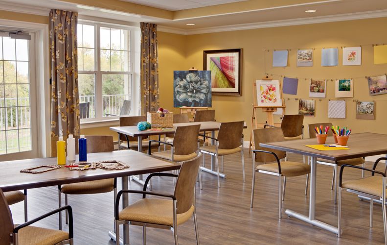 An art classroom with tables, chairs, and paintings displayed on easels.