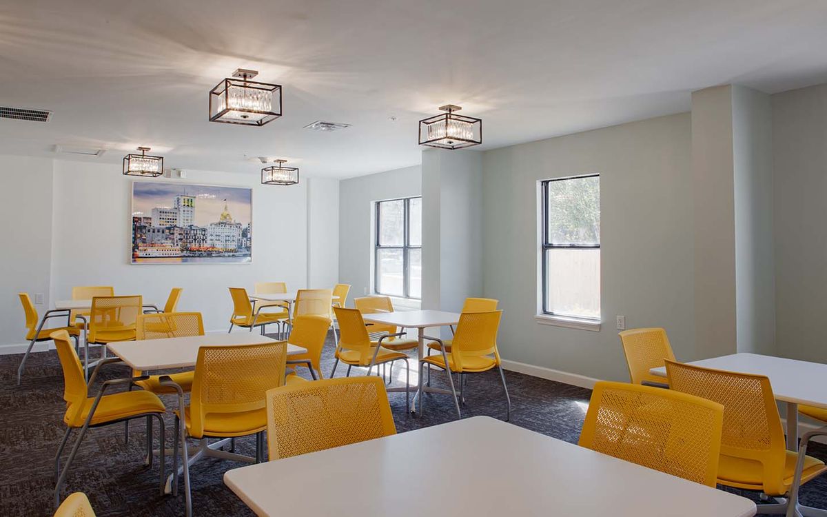 A modern dining area with yellow chairs and white tables, illuminated by natural light.