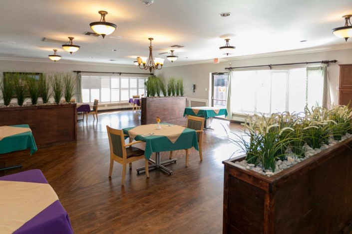A spacious dining area with neatly arranged tables and chairs, featuring wooden floors, large windows, and decorative plants.