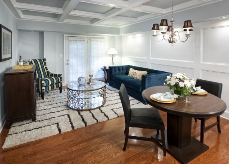 A stylish living room with a blue sofa, elegant coffee table, and adjacent dining area featuring a round table and chandelier.