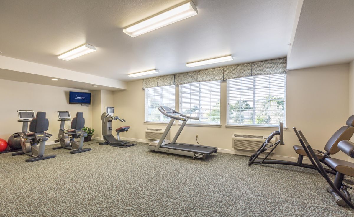 A well-lit gym room featuring various exercise equipment, including a treadmill and stationary bike.