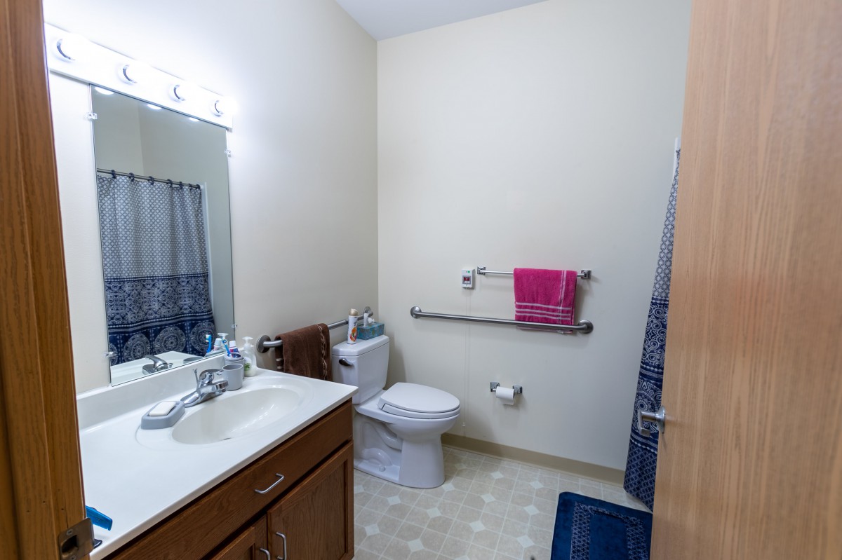A well-organized bathroom featuring a sink, toilet, and mirror with towels and a grab bar for accessibility.