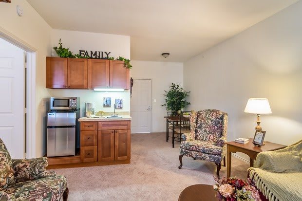 A cozy living area with a kitchenette, featuring wooden cabinets and floral-patterned armchairs.