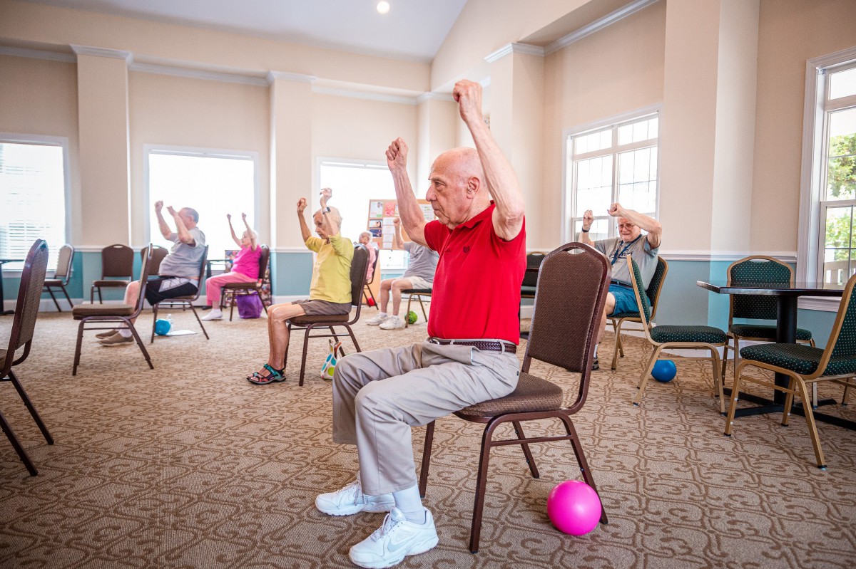 A group of seniors participating in a chair exercise class indoors, promoting health and wellness.